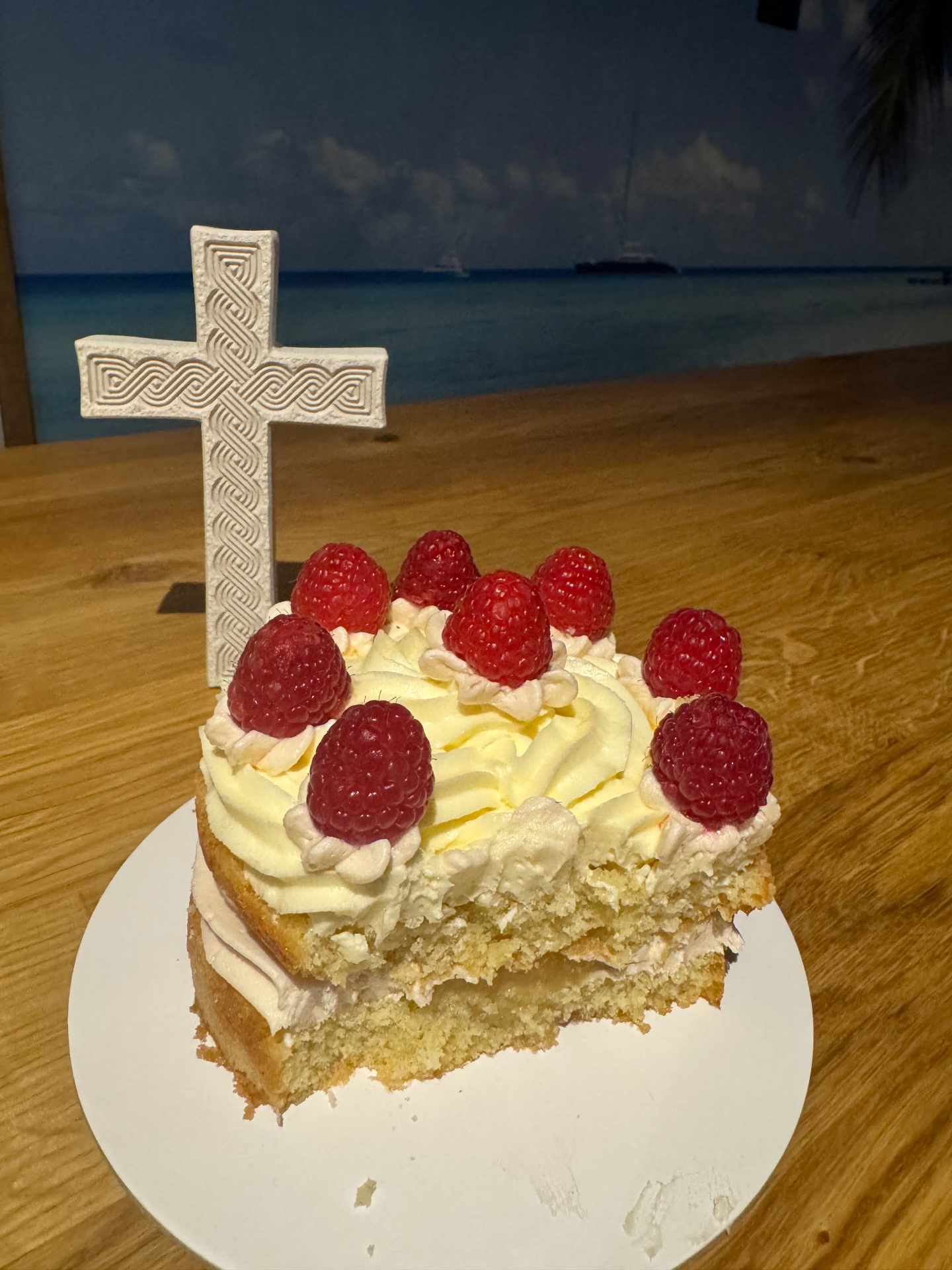 Raspberry-topped sponge cake with buttercream rosettes beside a white carved cross
