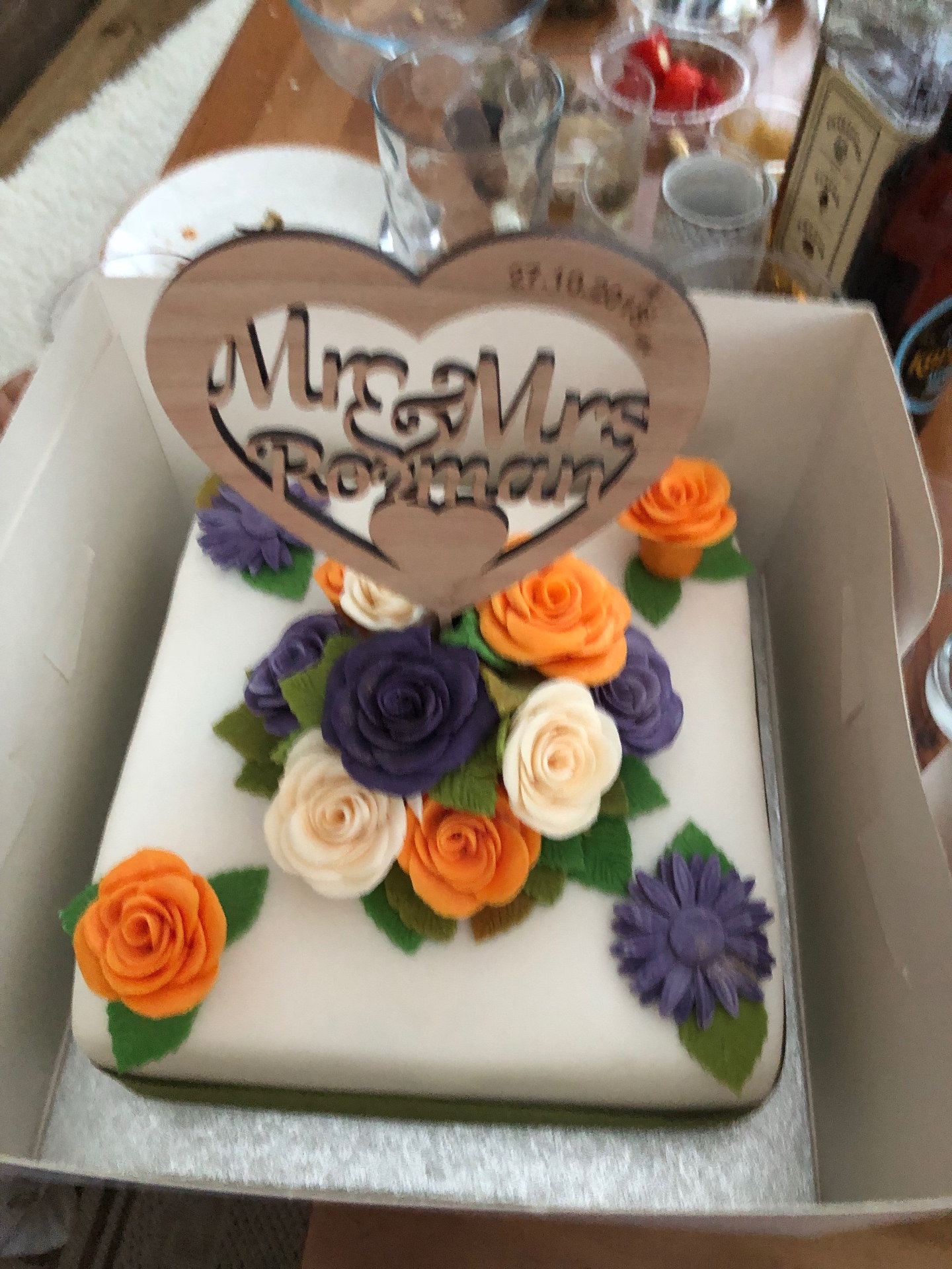 Square wedding cake with orange, purple, and ivory sugar roses and a wooden Mr & Mrs heart topper